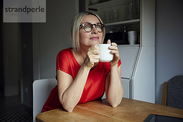 Nachdenkliche Frau mit Teetasse sitzt am Tisch