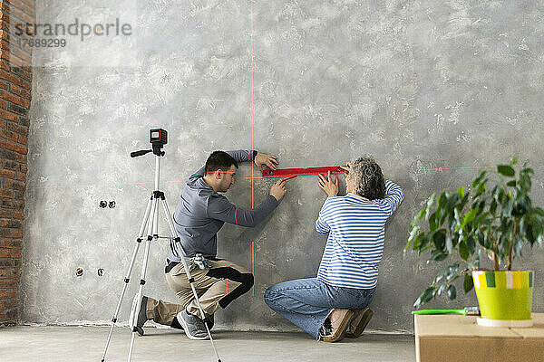Frau und Mann messen Baulaserniveau an grauer Wand