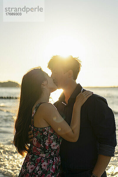 Junges Paar küsst sich an einem sonnigen Tag vor dem Meer
