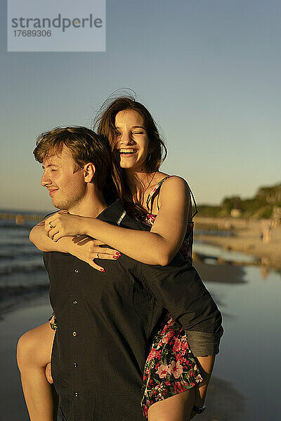 Mann gibt Frau am Strand bei Sonnenuntergang Huckepackfahrt