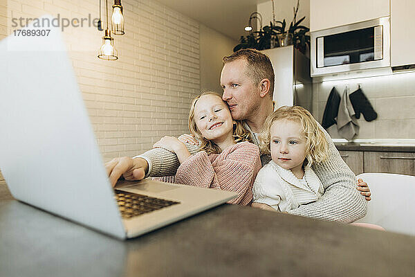 Lächelnder Geschäftsmann mit Töchtern  die zu Hause Laptop benutzen