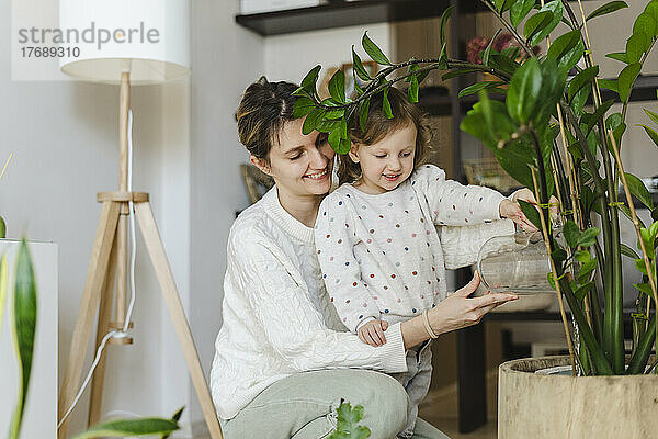 Lächelnde Mutter und Tochter gießen Pflanze zu Hause