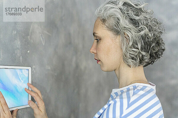 Frau mit grauem Haar benutzt Tablet-PC an der Wand