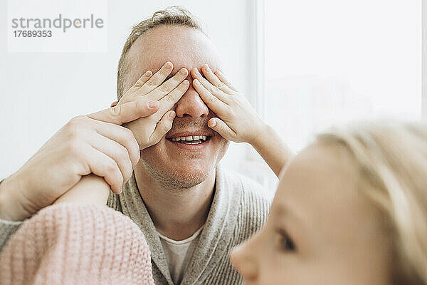 Daughter covering eyes of father with hands at home