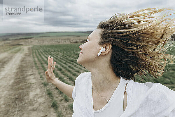 Sorglose Frau mit In-Ear-Kopfhörern tanzt auf einem landwirtschaftlichen Feld