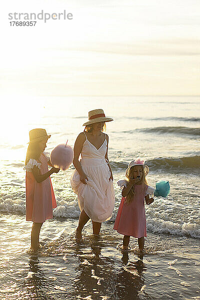 Mutter mit Töchtern isst an einem sonnigen Tag am Strand Zuckerwatte