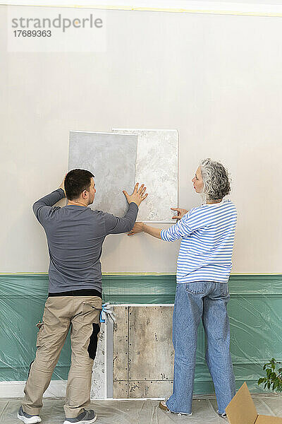 Frau und Freundin wählen Tapete aus Mustern auf weißer Wand aus