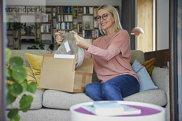 Lächelnde Frau überprüft zu Hause auf dem Sofa Kleidung im Paket