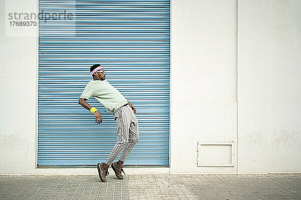 Flexibler junger Mann tanzt auf Fußweg vor blauem Fensterladen