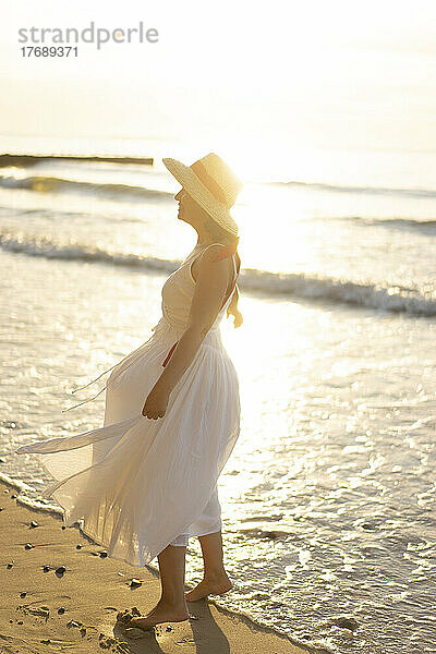 Frau mit Hut steht am Ufer am Strand