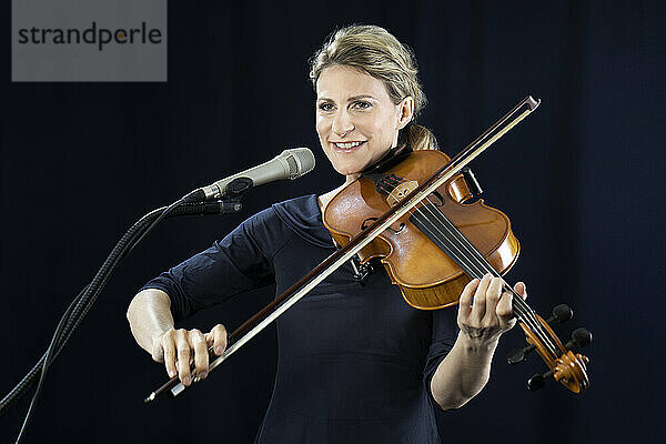 Lächelnde reife Frau  die vor schwarzem Hintergrund Geige spielt