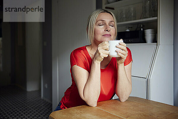 Reife Frau mit Teetasse am Tisch sitzend