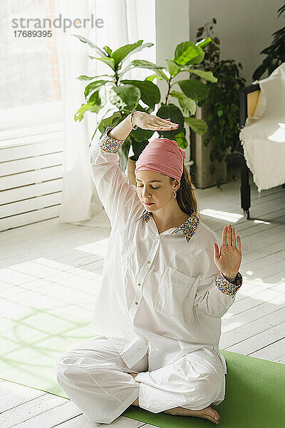 Frau mit erhobener Hand praktiziert Yoga zu Hause