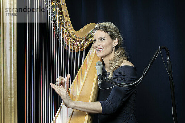 Lächelnde reife Frau spielt Harfe vor schwarzem Hintergrund
