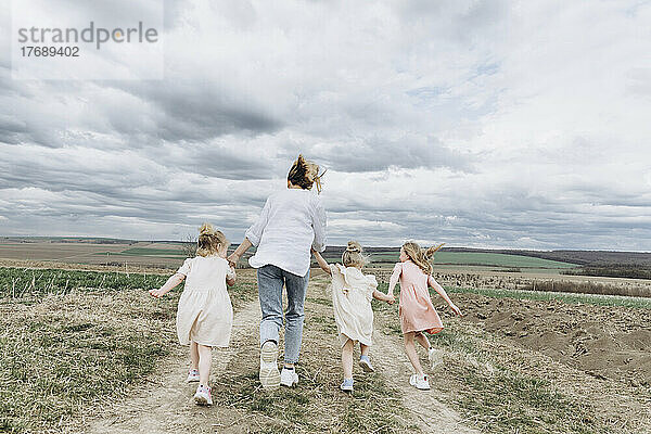 Frau mit drei Töchtern läuft auf einem landwirtschaftlichen Feld