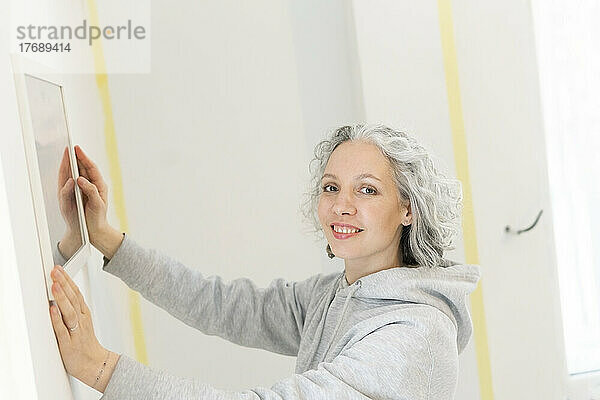 Lächelnde Frau arrangiert Spiegel an der Wand