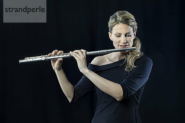 Reife Frau spielt Flöte vor schwarzem Hintergrund