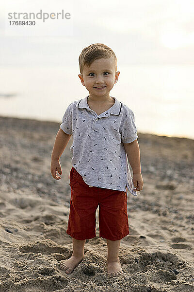 Lächelnder kleiner Junge steht am Strand
