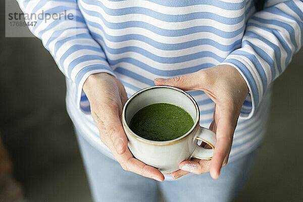 Hände einer Frau  die eine Tasse grünen Tee hält