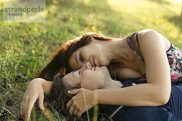 Lächelndes junges Paar  das an einem sonnigen Tag im Gras liegt