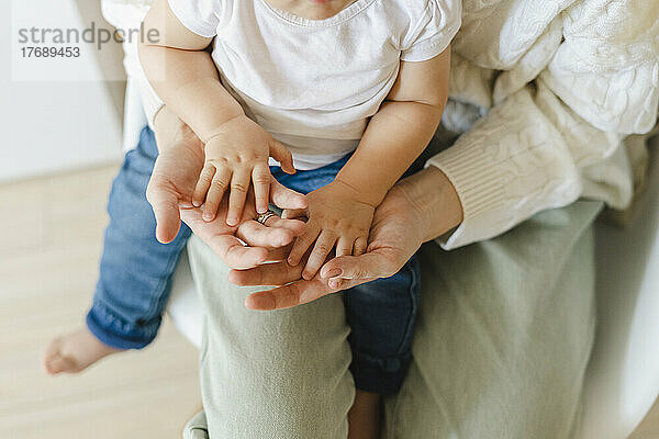 Ein kleiner Junge berührt die Hände seiner Mutter  die zu Hause auf ihrem Schoß sitzt