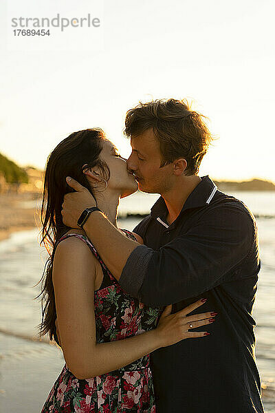 Zärtliches junges Paar küsst sich an einem sonnigen Tag am Strand