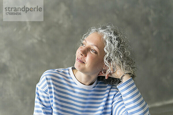 Lächelnde Frau mit grauen Haaren vor der Wand