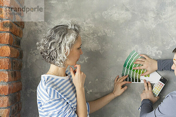 Frau mit Freundin wählt Farbe aus Farbmuster an grauer Wand