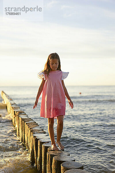 Nettes Mädchen  das auf einem Holzpfosten am Strand läuft