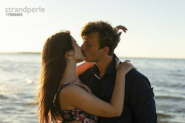 Young couple kissing each other in front of sea on sunny day