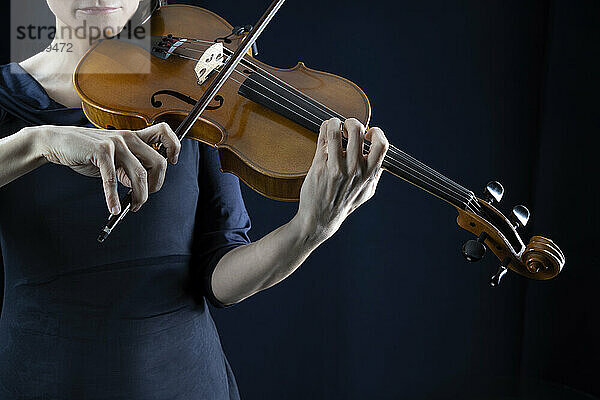 Reife Frau spielt Geige vor schwarzem Hintergrund