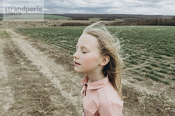 Mädchen mit geschlossenen Augen genießt den Wind im landwirtschaftlichen Feld