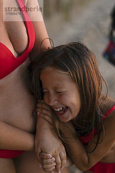 Fröhliche Tochter lacht mit Mutter am Strand