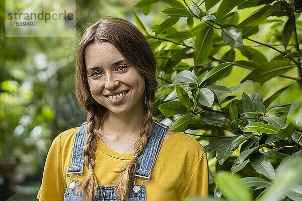 Lächelnde junge Frau steht neben der Pflanze im Garten