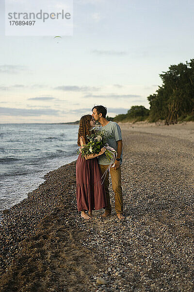 Mann küsst Frau am Strand auf die Stirn