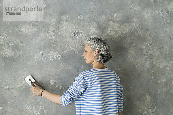 Frau mit Arbeitsgerät arbeitet an grauer Wand