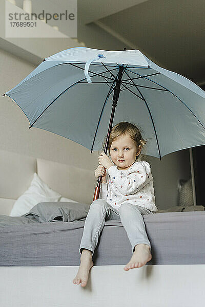 Unschuldiges Mädchen sitzt mit Regenschirm im Schlafzimmer