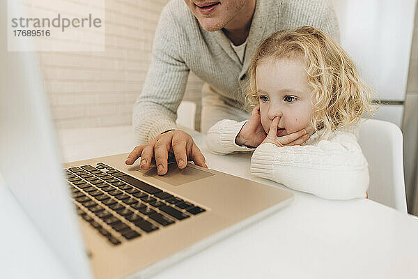 Nette Tochter mit Vater  der zu Hause Laptop benutzt