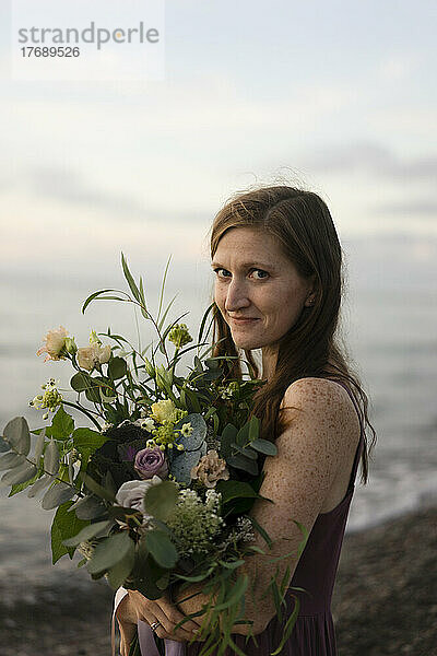 Lächelnde Frau mit Blumenstrauß am Strand