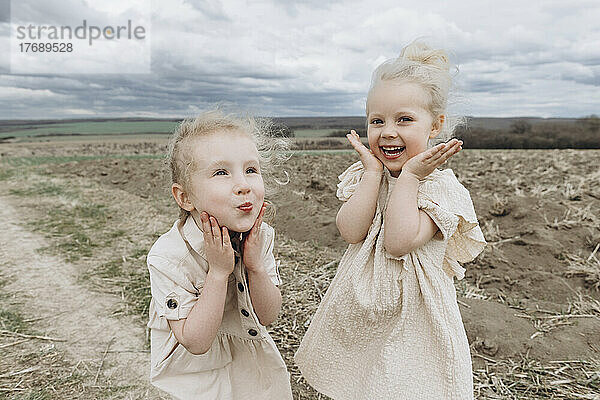 Cute happy sisters gesturing together at agricultural field
