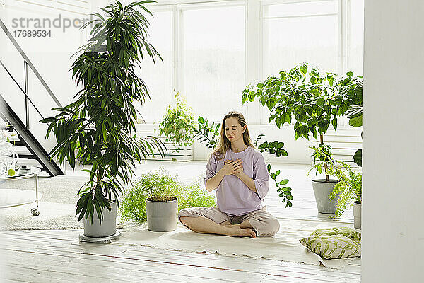 Frau sitzt zu Hause mit gekreuzten Beinen inmitten von Pflanzen