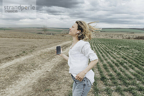 Lächelnde Frau  die im landwirtschaftlichen Bereich Musik hört