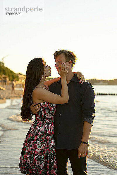 Junge Frau umarmt ihren Freund an einem sonnigen Tag am Strand des Meeres