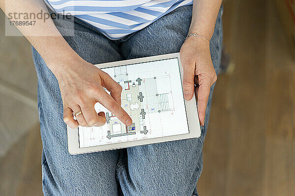 Hände einer Frau  die einen Tablet-PC hält und den Bauplan ihres Hauses untersucht
