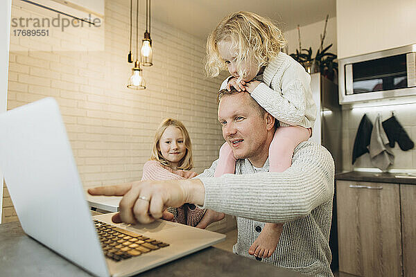 Mädchen sitzt auf der Schulter des Vaters und arbeitet zu Hause