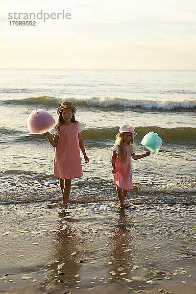 Geschwister mit Zuckerwatte stehen zusammen am Strand