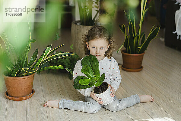 Unschuldiges Mädchen sitzt mit Topfpflanze im Wohnzimmer