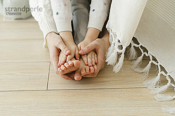 Mother's hand holding daughter's feet at home