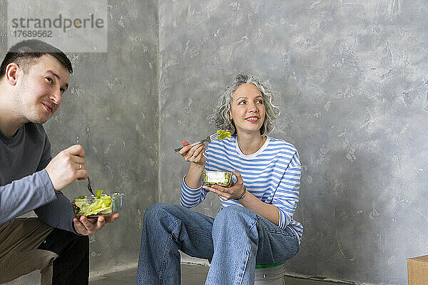 Glückliche Frau mit Freundin beim gemeinsamen Mittagessen vor der Wand sitzend