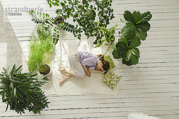 Frau entspannt sich zu Hause inmitten von Topfpflanzen